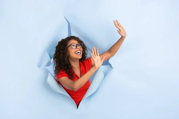 Veselá mladá žena pózuje v roztrhané modré papírové díře pozadí, emocionální a expresivní — Stock fotografie