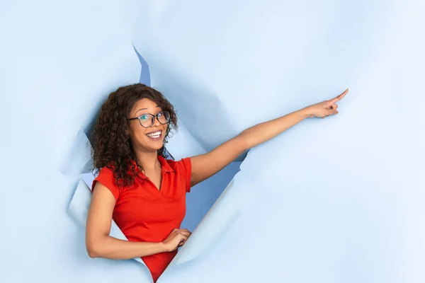Vrolijke jonge vrouw poseert in gescheurd blauw papier gat achtergrond, emotioneel en expressief — Stockfoto