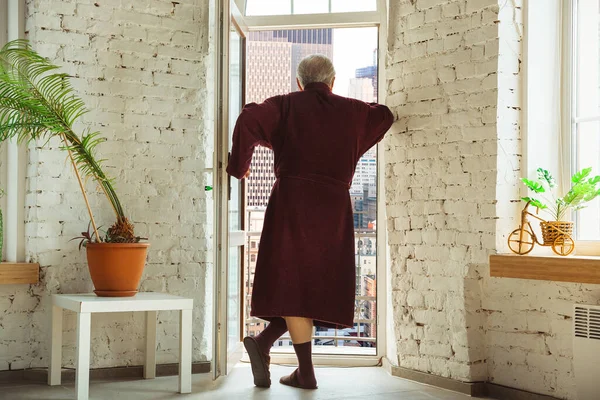 Homem idoso maduro durante a quarentena, percebendo o quão importante é ficar em casa durante o surto do vírus, olhando pela janela do dia Boston City — Fotografia de Stock