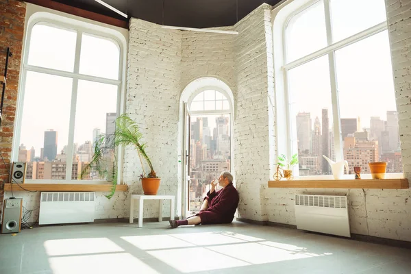 Hombre mayor maduro durante la cuarentena, dándose cuenta de lo importante que es quedarse en casa durante el brote de virus, mirando a través de la ventana del día Nueva York — Foto de Stock