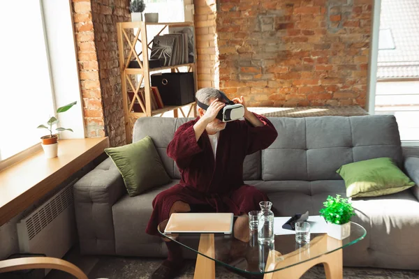 Dojrzały starszy mężczyzna podczas kwarantanny, uświadamiając sobie, jak ważne jest pozostanie w domu podczas epidemii wirusa, przymierzanie gogli VR, granie, oglądanie — Zdjęcie stockowe