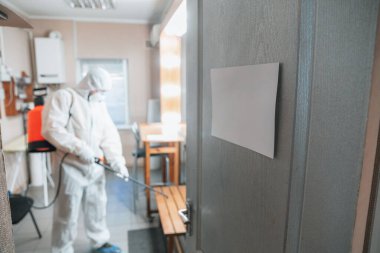 Koronavirüs salgını. Koruyucu giysinin içindeki bir dezenfektan evde ya da ofiste dezenfektan püskürtür.