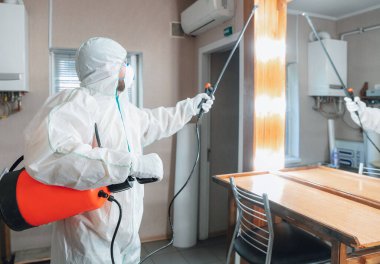 Koronavirüs salgını. Koruyucu giysinin içindeki bir dezenfektan evde ya da ofiste dezenfektan püskürtür.