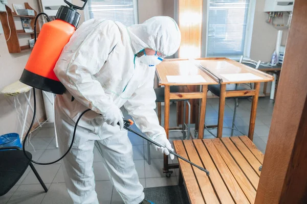 Coronavirus Pandemic. A disinfector in a protective suit and mask sprays disinfectants in the house or office — Stock Photo, Image