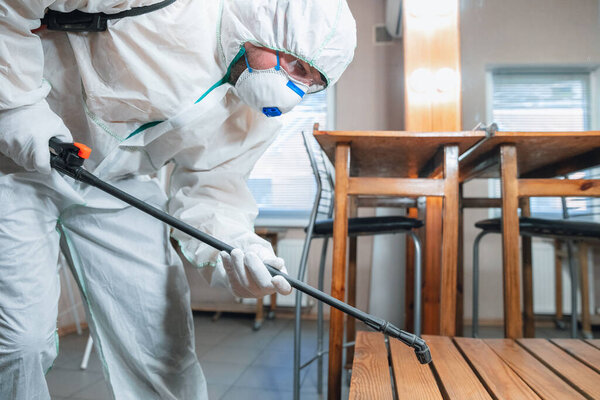 Пандемия коронавируса. Дезинфектор в защитном костюме и маска распыляет дезинфицирующие средства в доме или офисе
