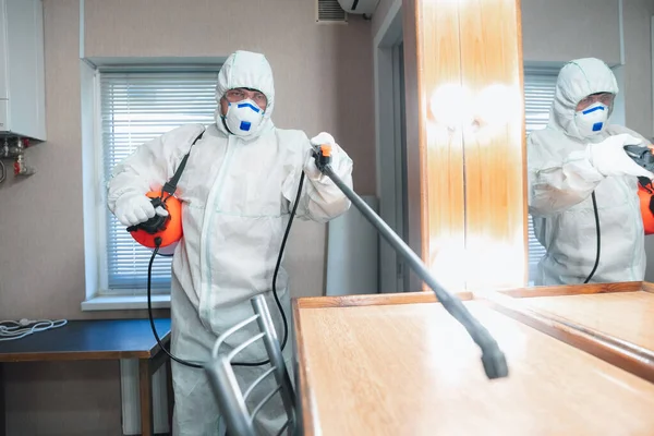 Coronavirus Pandemic. A disinfector in a protective suit and mask sprays disinfectants in the house or office — Stock Photo, Image