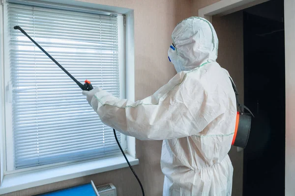 Koronavirová pandemie. Dezinfekce v ochranném obleku a masce rozstřikuje dezinfekční prostředky v domě nebo kanceláři — Stock fotografie