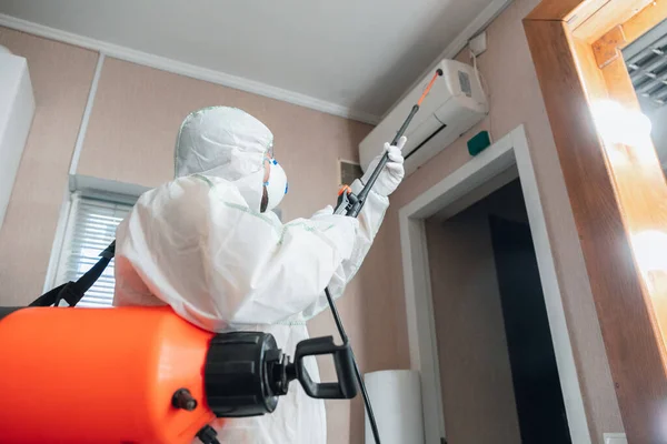 Coronavirus Pandemic. A disinfector in a protective suit and mask sprays disinfectants in the house or office — Stock Photo, Image