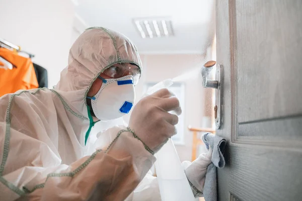 Coronavirus Pandemie. Een desinfector in een beschermend pak en masker spuit desinfecterende middelen in huis of op kantoor — Stockfoto