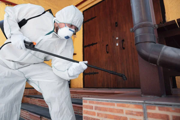 Coronavirus Pandemic. A disinfector in a protective suit and mask sprays disinfectants in the house or office — Stock Photo, Image