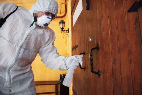 Pandémie de coronavirus. Un désinfecteur en combinaison de protection et un masque pulvérisent des désinfectants dans la maison ou le bureau — Photo