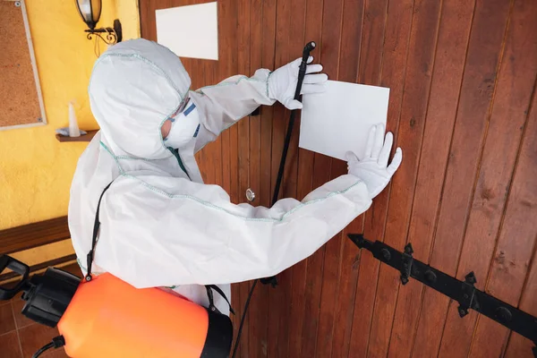 Pandémie de coronavirus. Un désinfecteur en combinaison de protection et un masque pulvérisent des désinfectants dans la maison ou le bureau — Photo