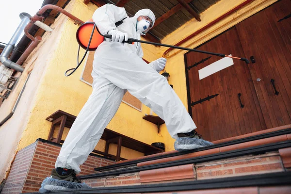 Coronavirus Pandemic. A disinfector in a protective suit and mask sprays disinfectants in the house or office — Stock Photo, Image