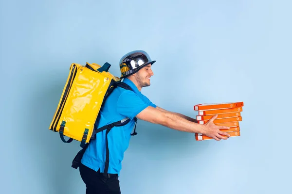 隔離中の非接触配送サービス。男は断熱材中に食品やショッピングバッグを提供します。青色の背景に隔離された配達人の感情. — ストック写真