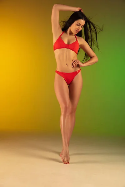 グラデーション緑黄色の背景にスタイリッシュな赤の高級水着で若いフィット感とスポーティ女性のファッション肖像画。夏の準備ができて完璧な体. — ストック写真