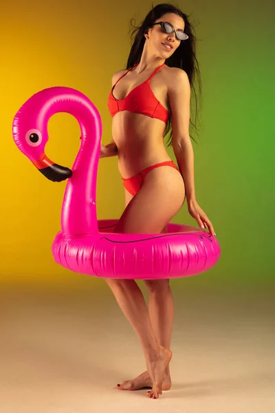 멋진 빨간색 호화 로운 수영복을 입은 젊은 여성의 패션 초상화와 단조 로운 배경에 고무 플라밍고가 그려져 있다. 여름을 대비 한 완벽 한 몸. — 스톡 사진