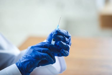 Ahşap masa arkasında şırıngalı mavi koruyucu eldivenler giyen doktorların ellerini kapatın.