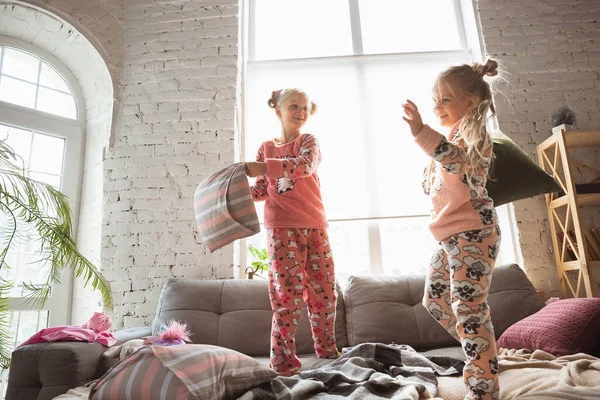 静かな小さな女の子はかわいいパジャマでベッドルームで遊んでいます,ホームスタイルと快適さ,笑いと戦う枕 — ストック写真