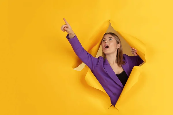 快乐的年轻女子在撕破的黄纸洞里摆出一副情绪化和表现力十足的样子 — 图库照片