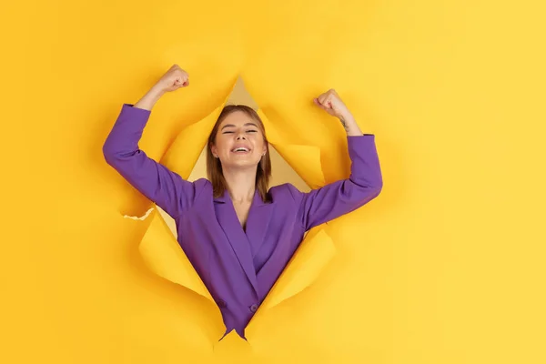 Fröhliche junge Frau posiert im zerrissenen gelben Papierlochhintergrund, emotional und ausdrucksstark — Stockfoto