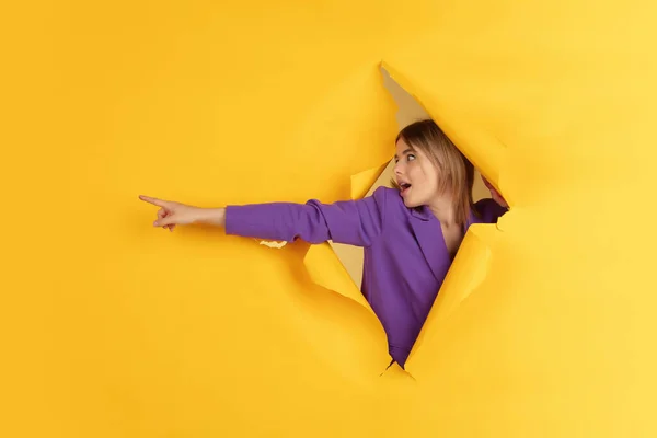 Fröhliche junge Frau posiert im zerrissenen gelben Papierlochhintergrund, emotional und ausdrucksstark — Stockfoto