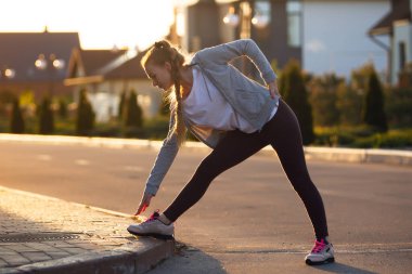 Genç bayan koşucu, gün ışığında şehir caddesinde koşmadan önce esneme hareketleri yapıyor. Güzel beyaz kadın eğitimi, müzik dinlemek.