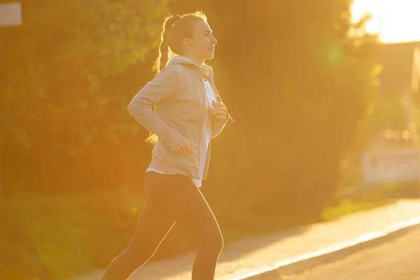 Jonge vrouwelijke loper, atleet is joggen in de stad straat in de zon. Mooie Kaukasische vrouw training, luisteren naar muziek — Stockfoto