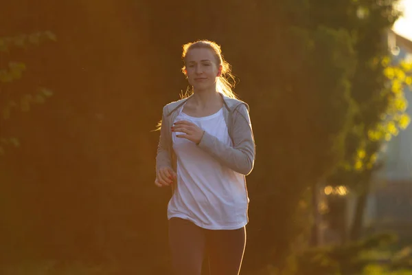Joven corredora, atleta está corriendo en la calle de la ciudad bajo el sol. Hermosa mujer caucásica entrenando, escuchando música — Foto de Stock