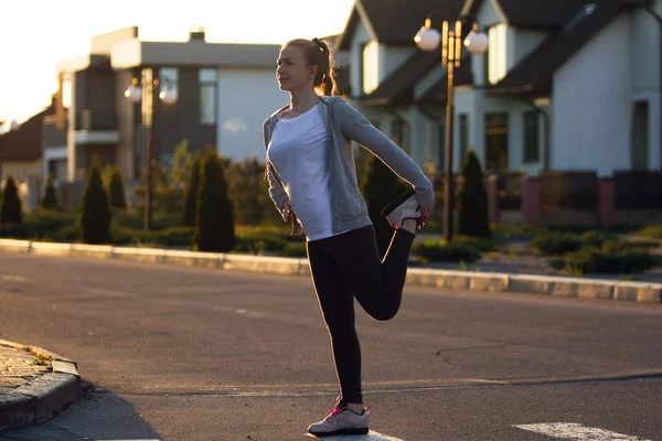 Jonge vrouwelijke loper, atleet is stretching voordat joggen in de stad straat in de zon. Mooie Kaukasische vrouw training, luisteren naar muziek — Stockfoto