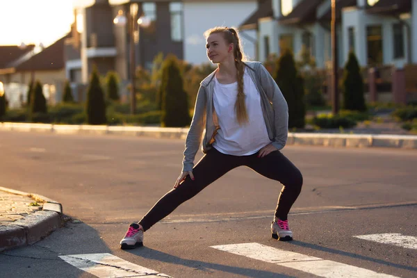 Jonge vrouwelijke loper, atleet is stretching voordat joggen in de stad straat in de zon. Mooie Kaukasische vrouw training, luisteren naar muziek — Stockfoto