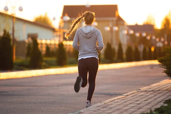 Jonge vrouwelijke loper, atleet is joggen in de stad straat in de zon. Mooie Kaukasische vrouw training, luisteren naar muziek — Stockfoto