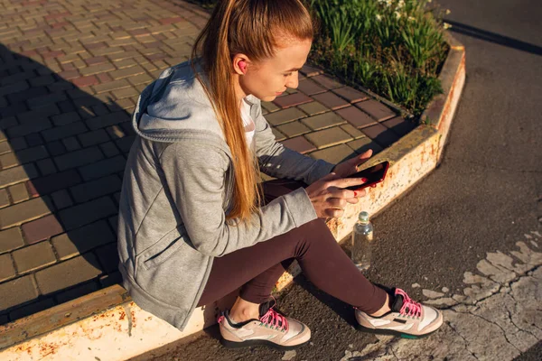 Mladá běžkyně, sportovkyně odpočívající po běhání na městské ulici na sluníčku. Krásná běloška trénink, poslech hudby — Stock fotografie