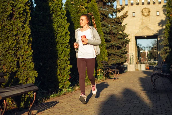 Joven corredora, atleta está corriendo en la calle de la ciudad bajo el sol. Hermosa mujer caucásica entrenando, escuchando música — Foto de Stock