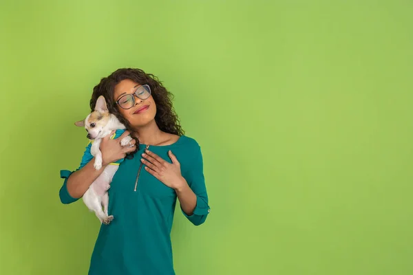 Afro-Amerikalı güzel genç kadın portresi yeşil stüdyo arka planında küçük köpekli, duygusal ve anlamlı. Reklam için kopyalama alanı. — Stok fotoğraf