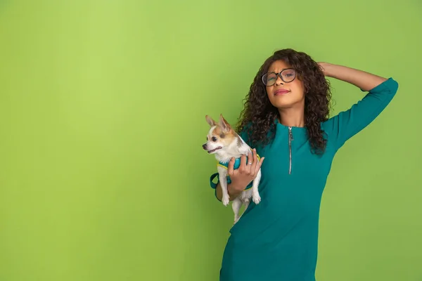 Afro-Amerikalı güzel genç kadın portresi yeşil stüdyo arka planında küçük köpekli, duygusal ve anlamlı. Reklam için kopyalama alanı. — Stok fotoğraf