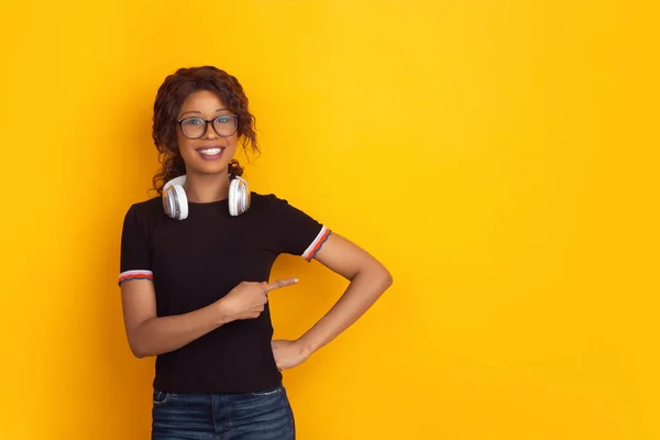 Afro-americanos hermosas mujeres jóvenes retrato con auriculares inalámbricos en fondo de estudio amarillo, emocional y expresivo. Copyspace para anuncio . — Foto de Stock