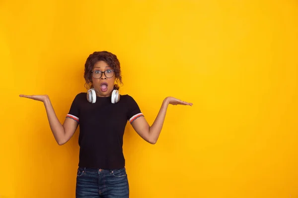 Afroameričanky krásné mladé ženy portrét s bezdrátovými sluchátky na žlutém pozadí studia, emocionální a expresivní. Kopírovací prostor pro reklamu. — Stock fotografie