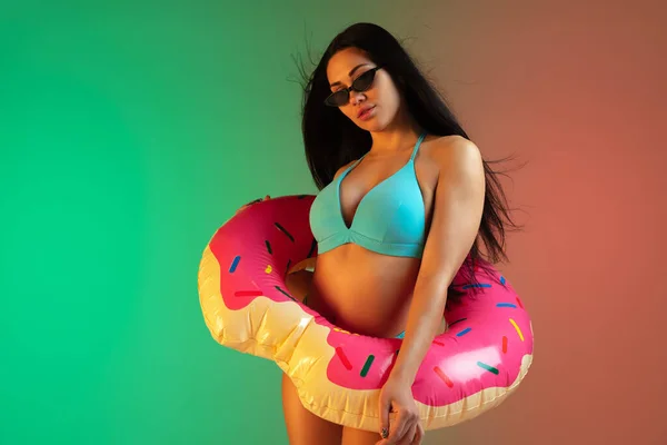 Retrato de moda de mulher jovem em forma e esportiva em roupa de banho de luxo azul com donut de borracha e óculos de sol elegantes no fundo gradiente. Corpo perfeito pronto para o verão . — Fotografia de Stock