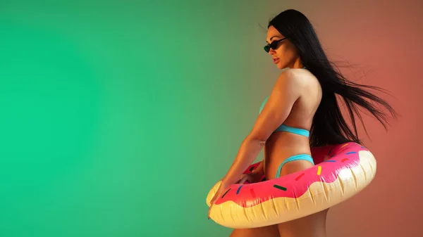Modeporträt einer jungen, fitten und sportlichen Frau in blauer Luxus-Badebekleidung mit Gummi-Donut und stylischer Sonnenbrille auf Steigungsuntergrund. Perfekter Körper, bereit für den Sommer. Flyer. — Stockfoto