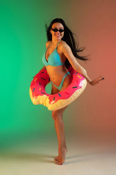 Modeporträt einer jungen, fitten und sportlichen Frau in blauer Luxus-Badebekleidung mit Gummi-Donut und stylischer Sonnenbrille auf Steigungsuntergrund. Perfekter Körper bereit für den Sommer. — Stockfoto
