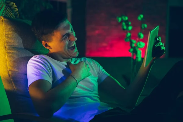 Fényképes portré egy jóképű fiatalemberről, aki eszközöket használ, kütyü a neon megvilágított belsejében. Ifjúsági kultúra, élénk színek — Stock Fotó