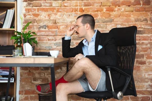 Young man without pants but in jacket working on a computer, laptop. Remote office during coronavirus, fun and comfortable work in underpants — Stock Photo, Image