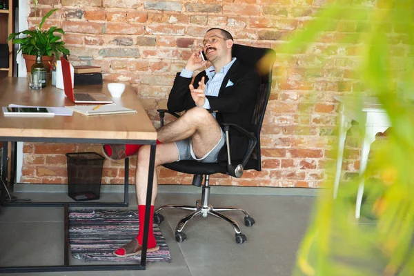 Young man without pants but in jacket working on a computer, laptop. Remote office during coronavirus, fun and comfortable work in underpants