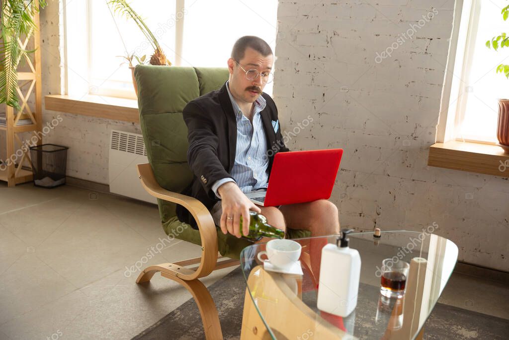 Young man without pants but in jacket working on a computer, laptop. Remote office during coronavirus, fun and comfortable work in underpants