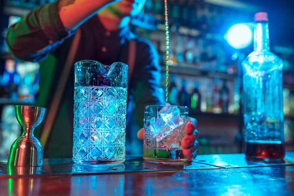Крупный план бармена заканчивает подготовку алкогольного ликера и ледяного коктейля в разноцветном неоновом свете — стоковое фото