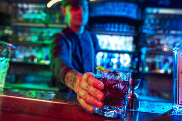Nahaufnahme vom Barmann beendet die Zubereitung eines alkoholischen Cocktails in buntem Neonlicht — Stockfoto