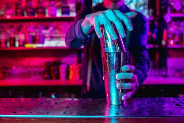Крупный план бармена завершает подготовку алкогольного коктейля с шейкером в разноцветном неоновом свете — стоковое фото