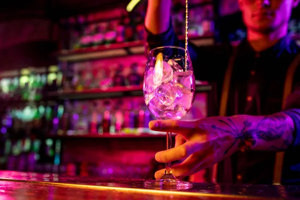 Nahaufnahme des Barmanns beendet die Zubereitung eines alkoholischen Cocktails, indem er das Getränk in buntes Neonlicht gießt — Stockfoto