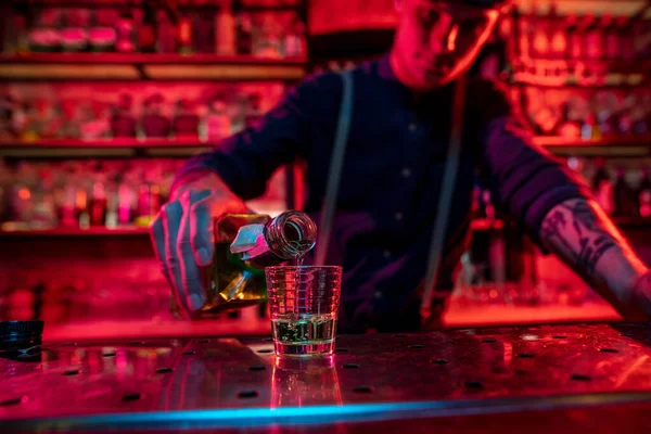 Бармен заканчивает подготовку алкогольного коктейля, наливает напиток в разноцветный неоновый свет, фокусируется на стекле — стоковое фото