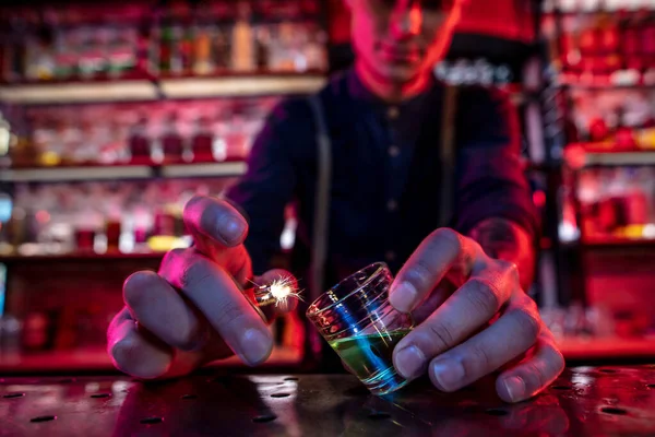 Barmann beendet die Zubereitung eines alkoholischen Cocktails, setzt Feuer, um es in buntem Neonlicht zu trinken, konzentriert sich auf Glas — Stockfoto